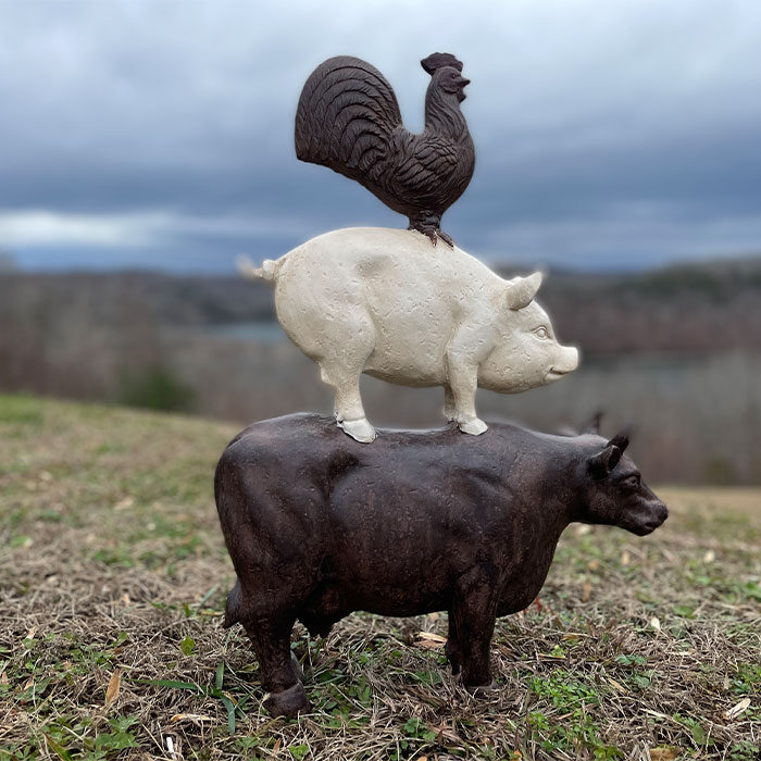 A black and white stone decoration depicts a rooster on top of a pig on top of a cow.