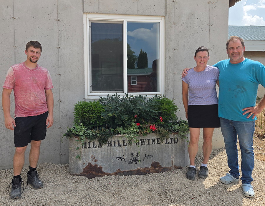 Three people stand smiling in front of a window and a planter labeled "Mill Hill's Wine Ltd.