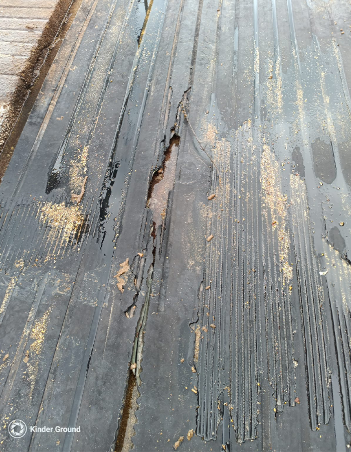 A damaged rubber mat with large cracks and peeling, with sand and water on its surface.