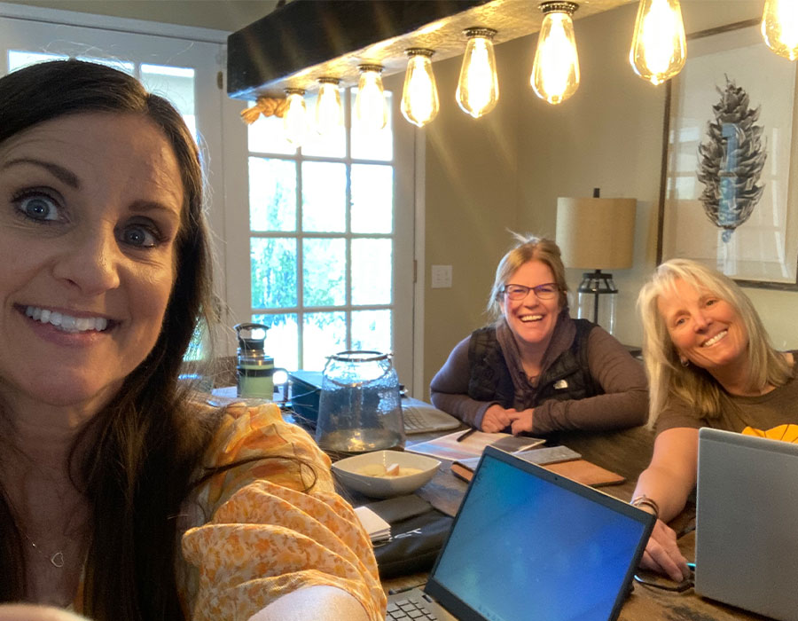 Co-Founders of Kinder Ground Dr. Jen Walker, Dr. Cassandra Tucker, and Lisa Cranfill sit around a cluttered table with laptops.