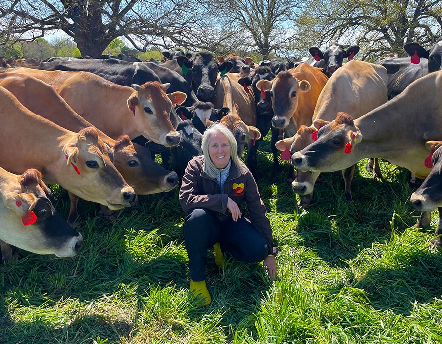 Kinder Ground co-founder Dr. Jen smiles n the centre of a circle of brown and black cows.